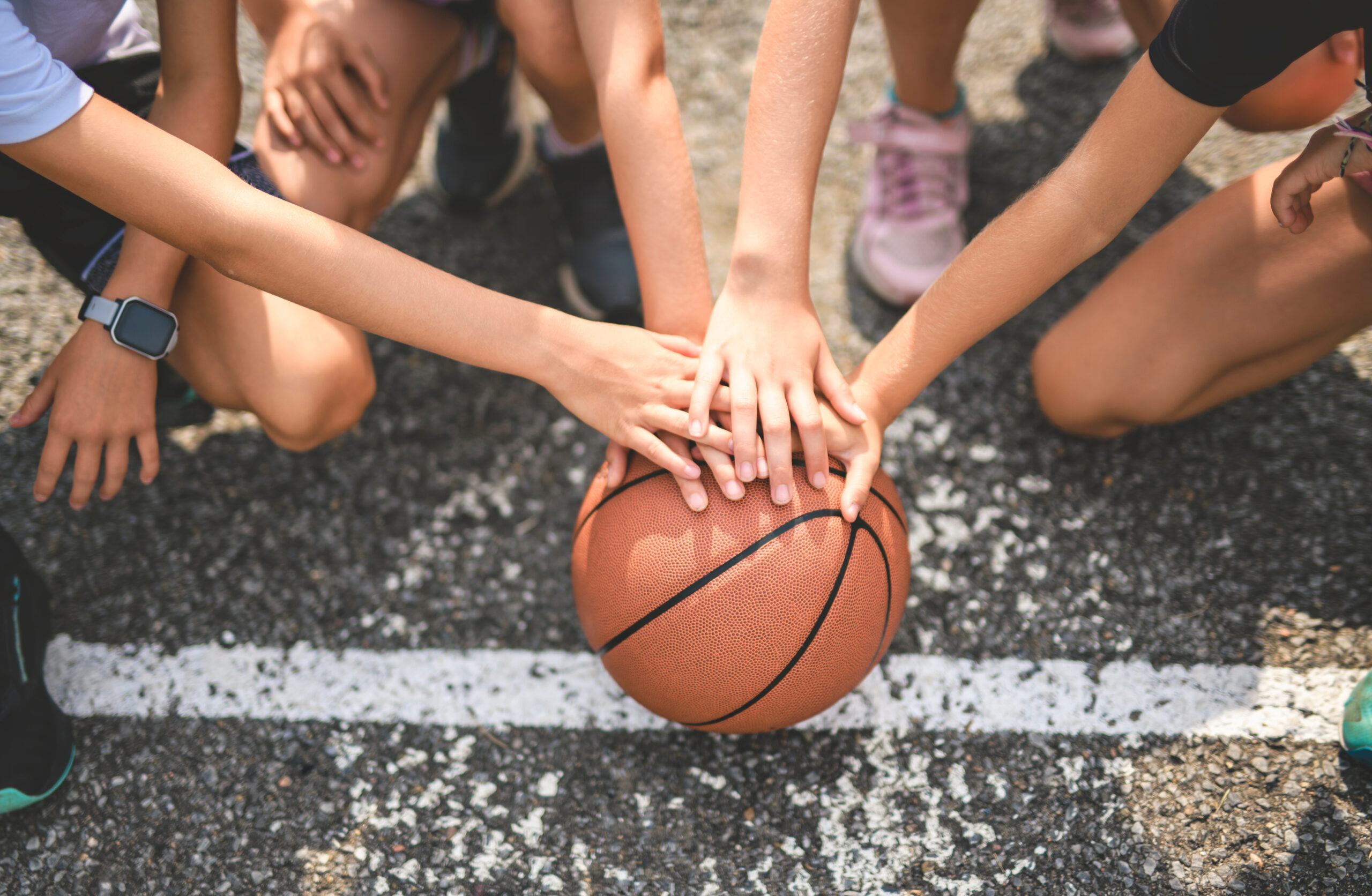 Youth players stack hands on a basketball outdoors during SCBL Programs, reflecting teamwork, skill development, and competitive training sessions.
