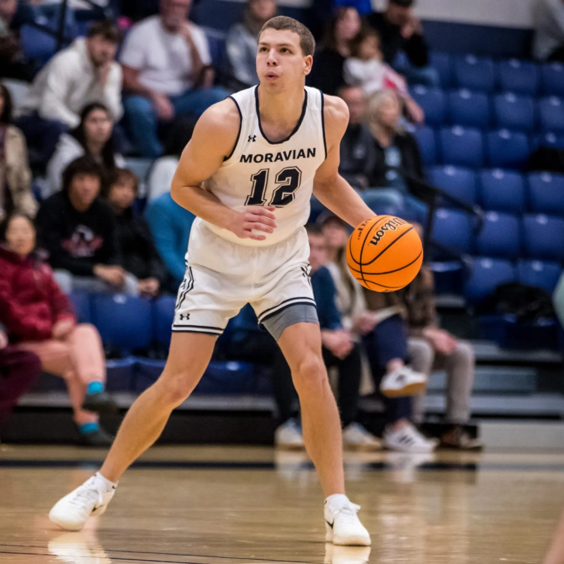 During a Moravian basketball game, Chad Kratzer dribbles in a white number 12 jersey as SCBL youth hoops context references the Lehigh Valley.