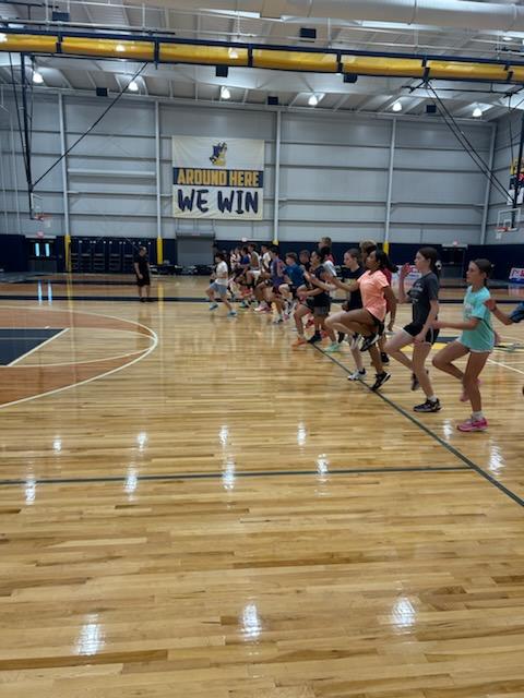 During SCBL Gallery moments, players line up for a basketball drill on the court inside the gym during a team practice under bright lights together.