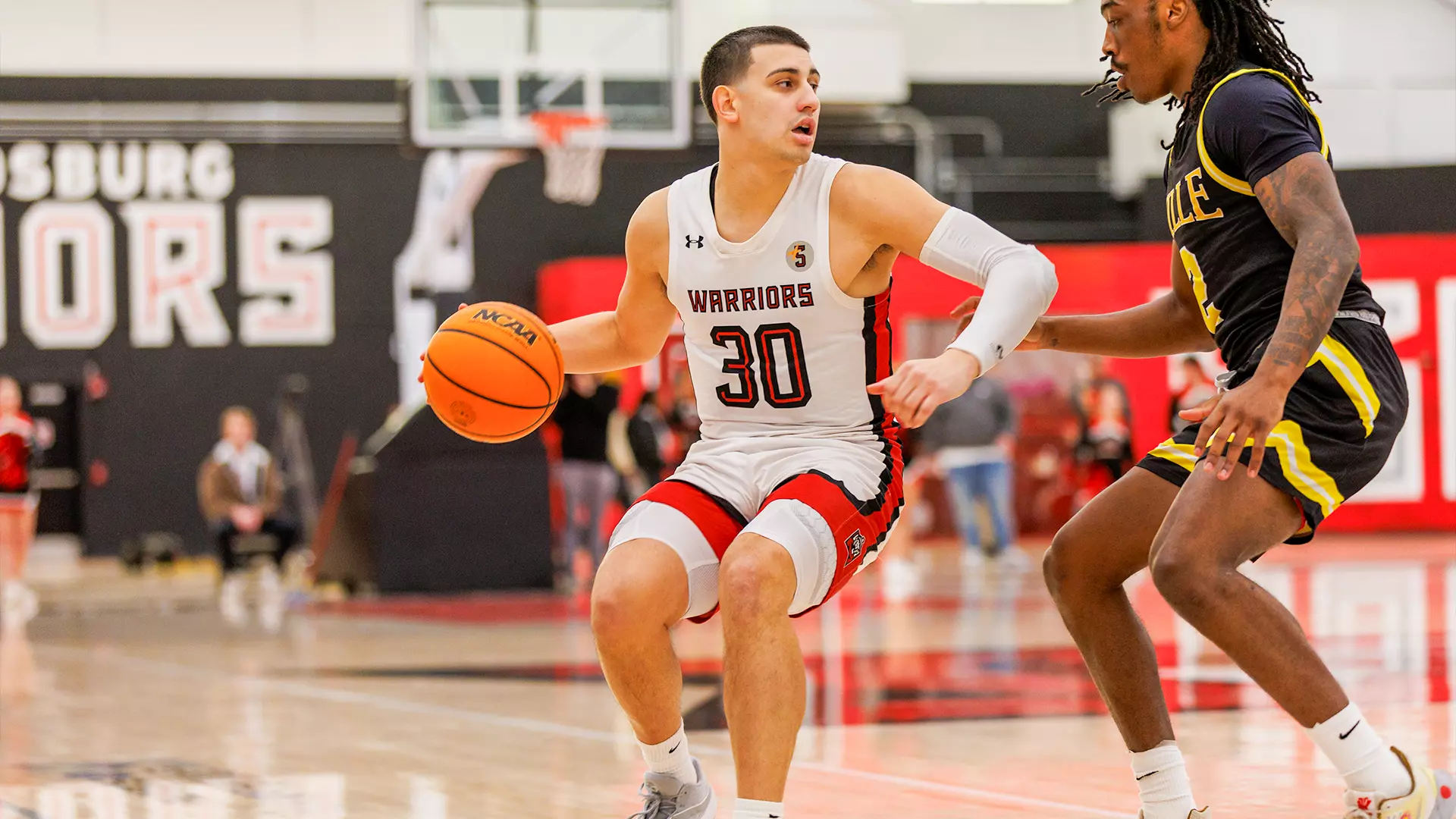 In the SCBL about page, Justin Paz controls the ball in a youth basketball matchup while a defender closes in during play at the gym.