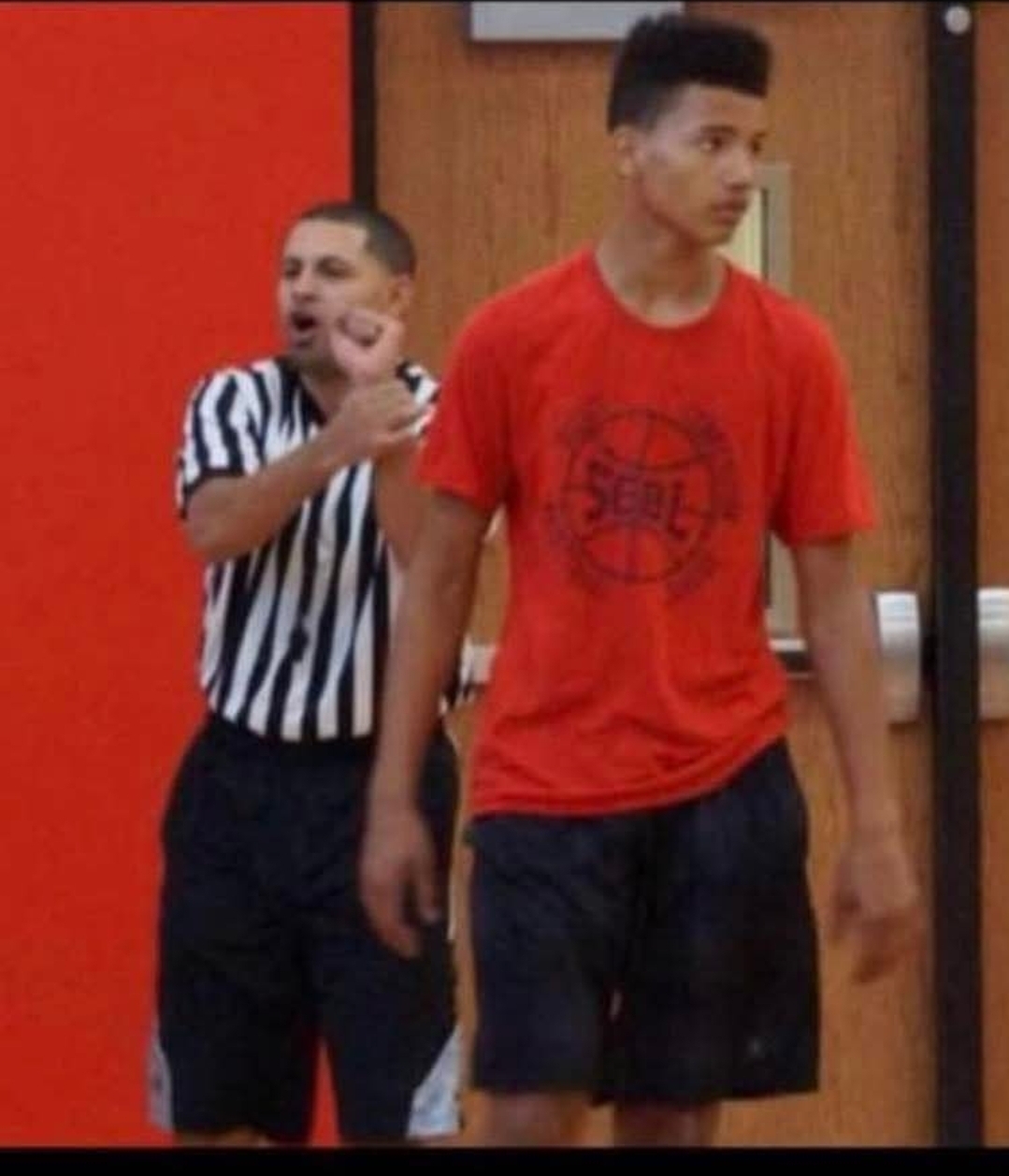 A referee signals beside a tall SCBL player in a red shirt during a youth basketball game in the Lehigh Valley, reflecting team competition and growth.