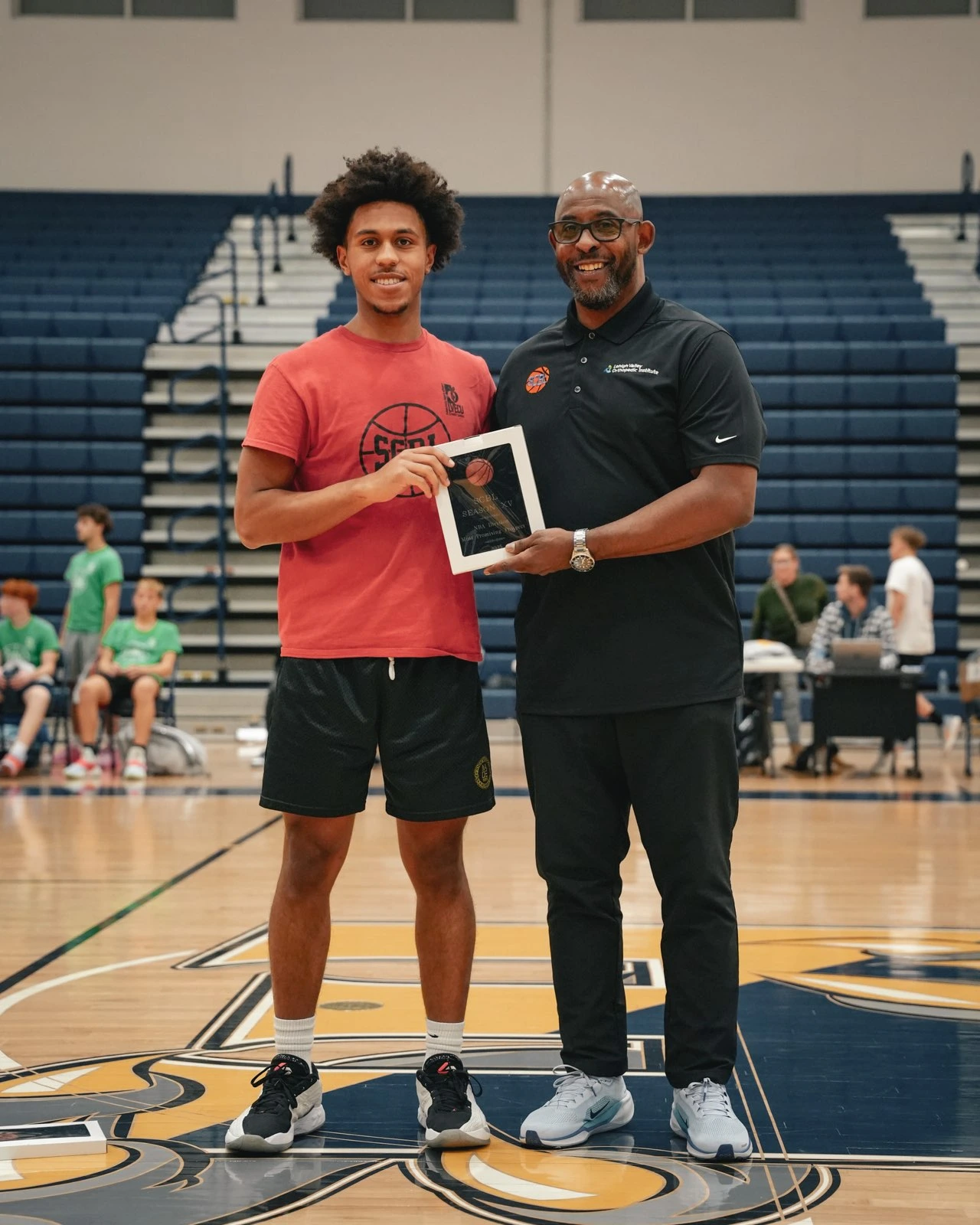 A SCBL youth basketball player and coach stand on the court in the Lehigh Valley after a recognition presentation during a gym event.