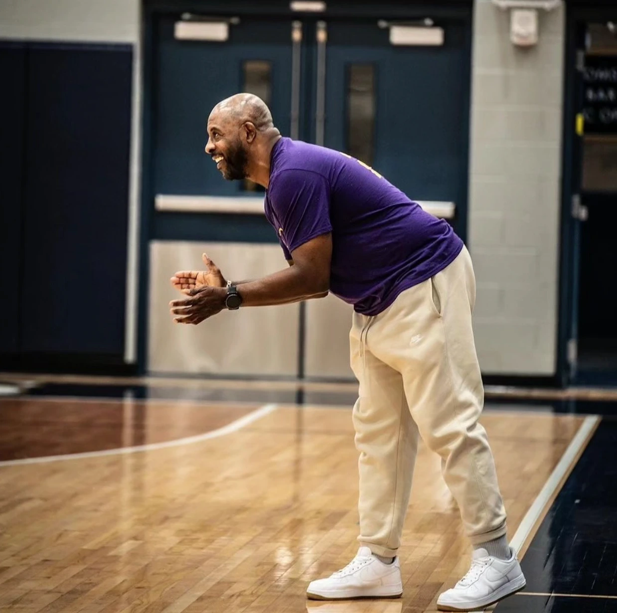 SCBL coach in a purple shirt claps on the basketball court during a youth programs session, encouraging players through teamwork and growth.